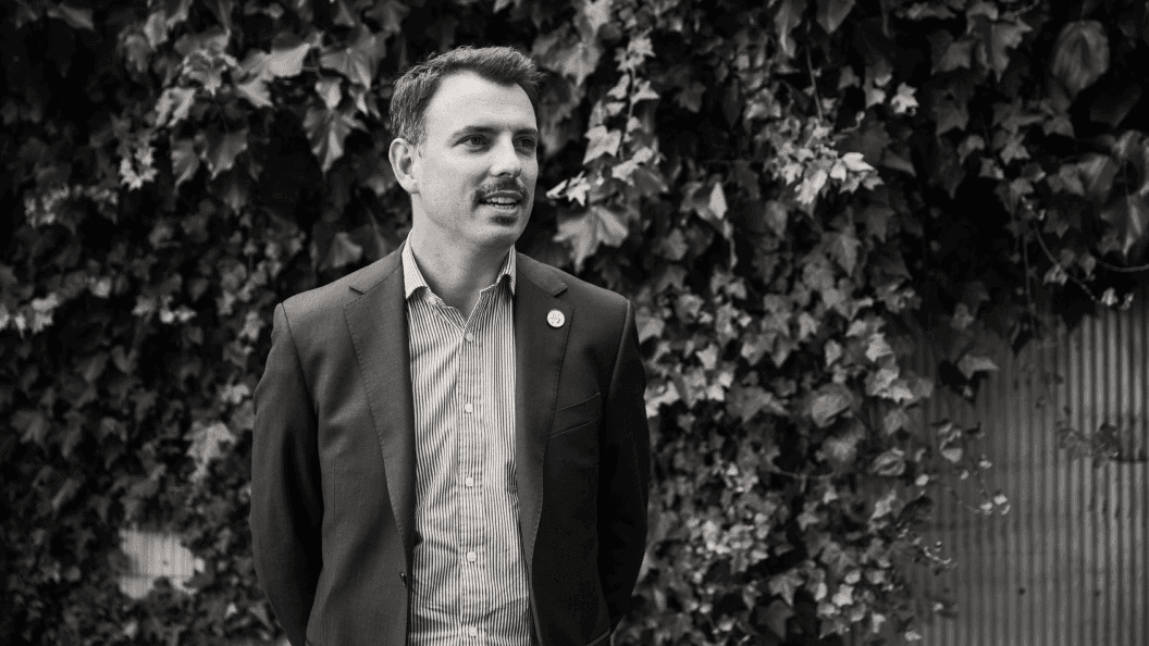 Young man in casual suit standing against a wall of vines