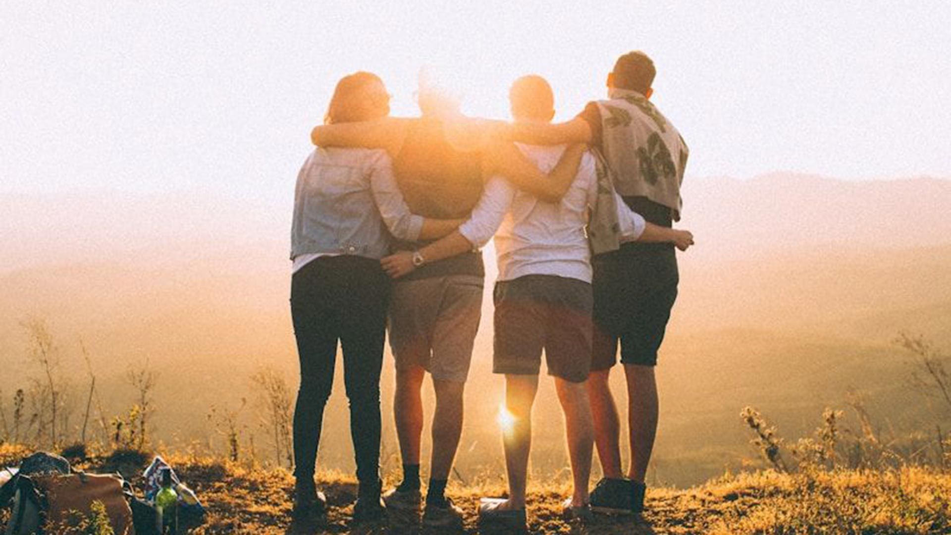 Photo showing a group of people with arms locked, looking into the sunset.