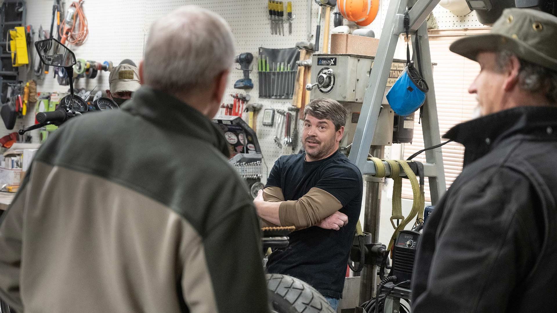 Photo showing three men chatting inside an automotive workshop.