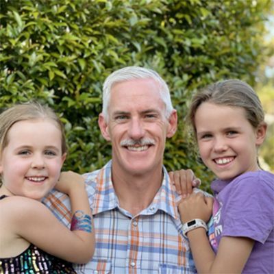 Grey-haired man smiling to camera, flanked by two smiling children.
