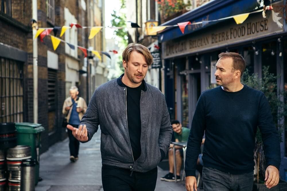 Two men walking side by side along a street, deep in conversation.