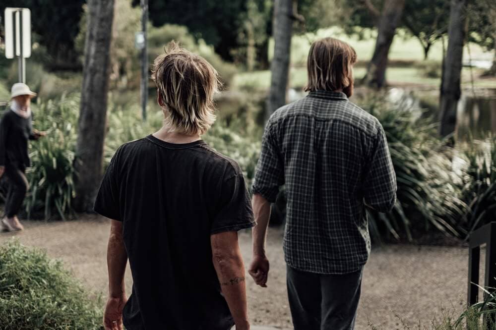 Two men walking side by side through a park, seen from behind.