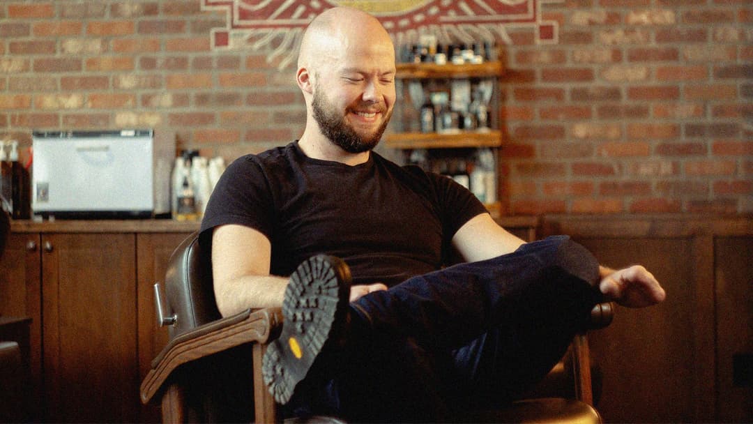 Photo d’un homme souriant qui regarde vers le bas, assis dans un fauteuil de barbier