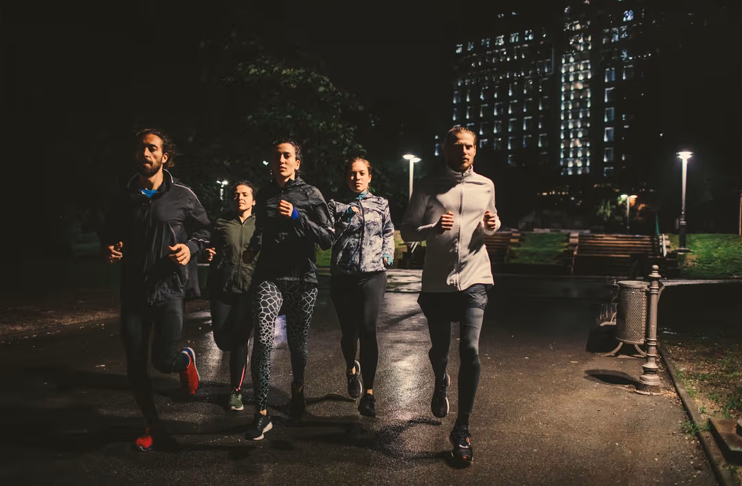 A group of people are running together through a park at night time