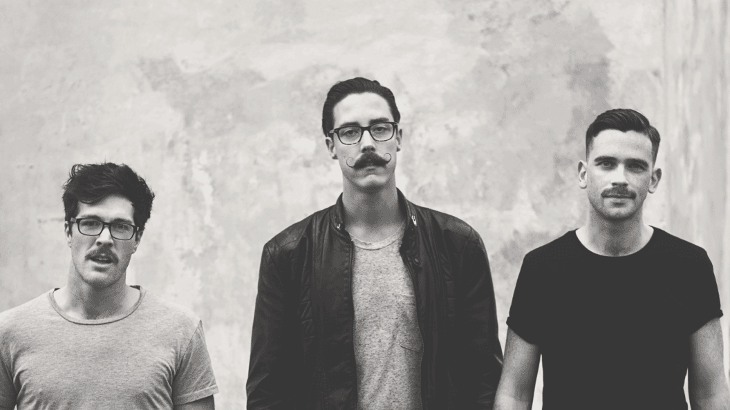 Portrait of three men with moustaches against concrete wall