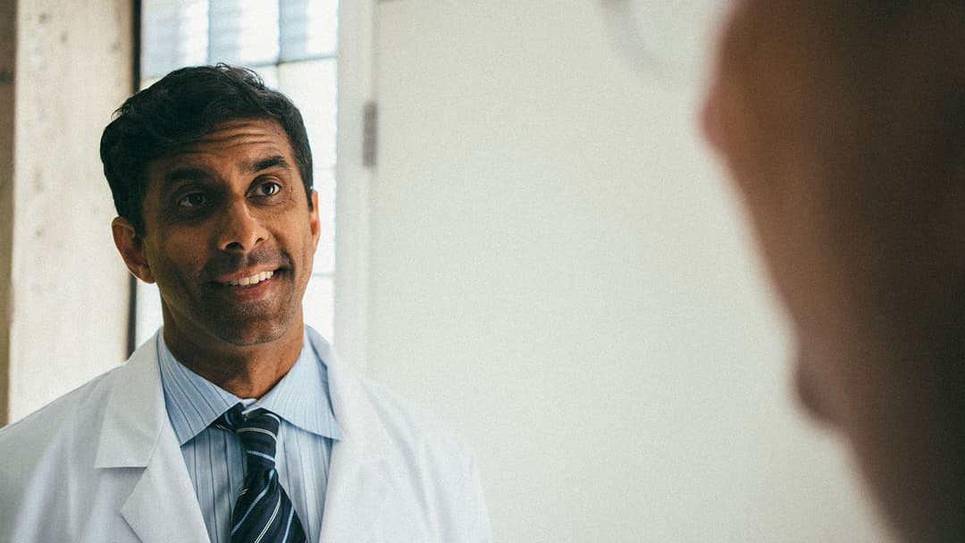 Photo of trustworthy-looking doctor in white medical coat, talking to camera.