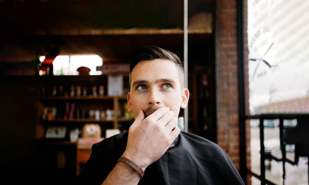 A man in a barber chair is stroking his moustache.