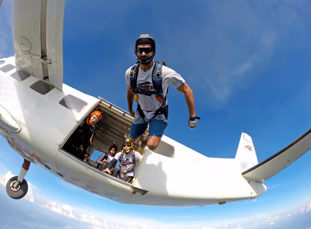 A man is jumping out of a plane wearing a skydiving gear