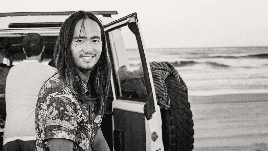 Man with long hair at the beach with a four wheel drive vehicle