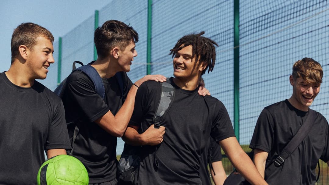 A photo of four young men walking and smiling with a football in hand.