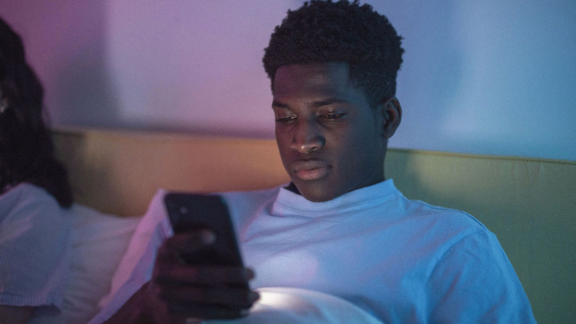 Photo of a young man in a dim room, engrossed in his smartphone.